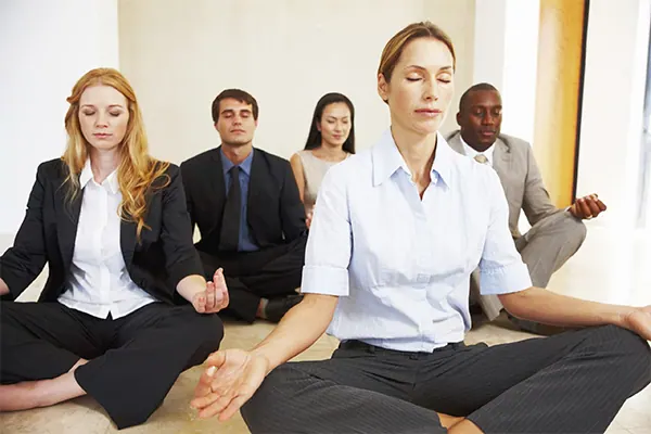 A group of office workers in business clothes meditating cross-legged on the floor