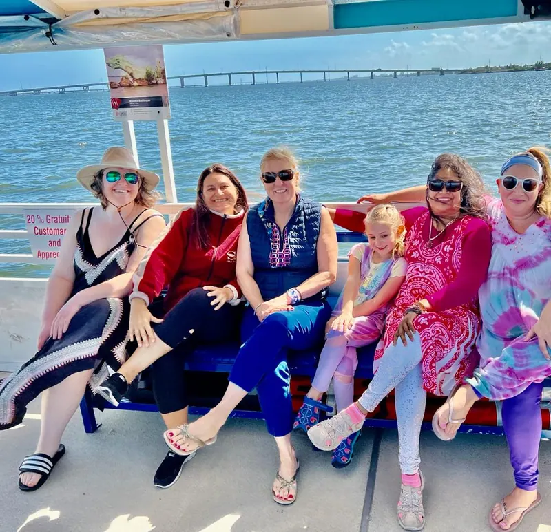 Six women and a child seated together on a boat bench at the waterfront