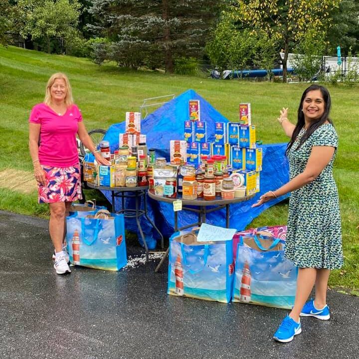 Bhavna Srivastava and a volunteer beside tables of donated tinned food for Saving People Inc.
