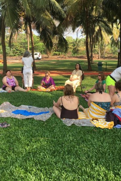 A group practising yoga on mats on the grass under palm trees